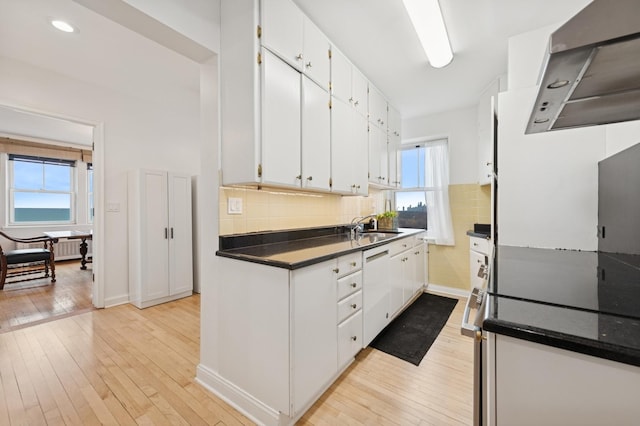 kitchen with white cabinets, backsplash, dishwasher, light wood finished floors, and dark countertops