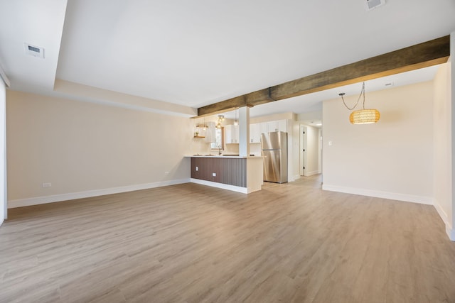 unfurnished living room featuring baseboards, visible vents, beamed ceiling, and light wood finished floors