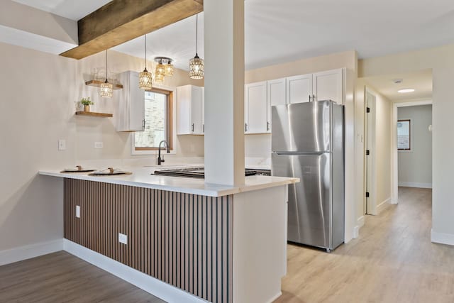 kitchen featuring light wood-style flooring, a peninsula, white cabinets, light countertops, and freestanding refrigerator