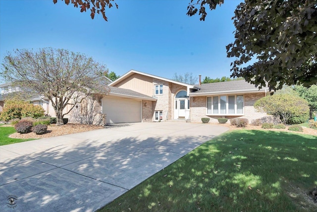 tri-level home featuring an attached garage, driveway, brick siding, and a front yard