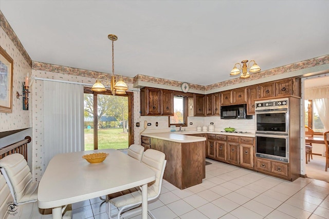 kitchen featuring light countertops, double oven, black microwave, a peninsula, and wallpapered walls