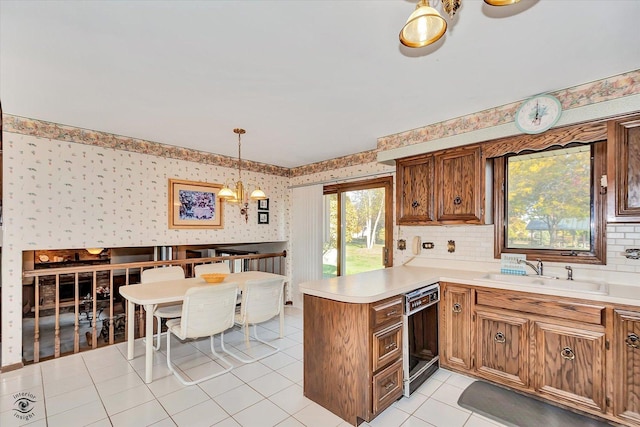 kitchen with a peninsula, a sink, light countertops, dishwasher, and wallpapered walls