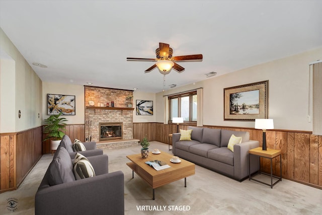 living room featuring light carpet, a ceiling fan, a wainscoted wall, wood walls, and a brick fireplace