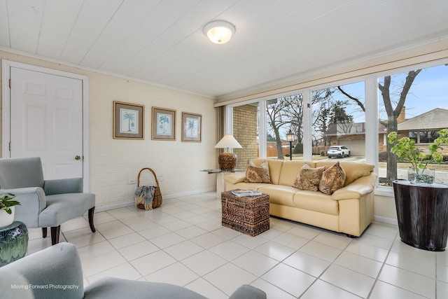 living area with light tile patterned floors, brick wall, ornamental molding, and baseboards