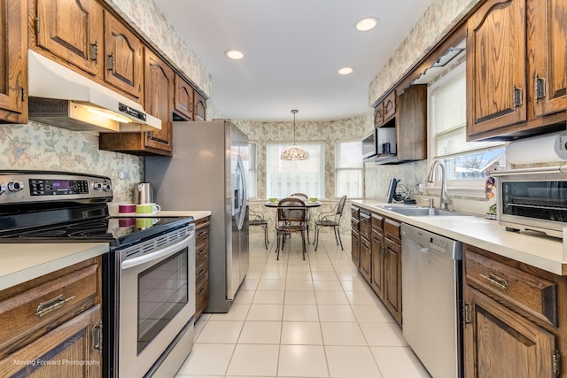 kitchen with light countertops, appliances with stainless steel finishes, a sink, and under cabinet range hood