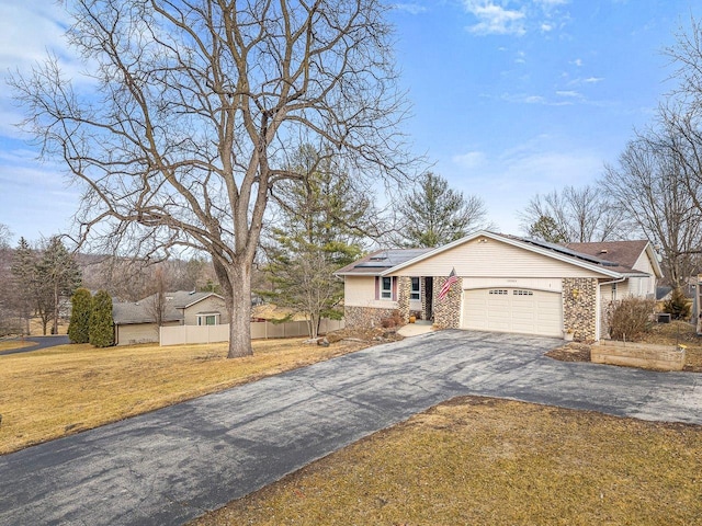 view of front of home featuring aphalt driveway, roof mounted solar panels, fence, a front yard, and an attached garage