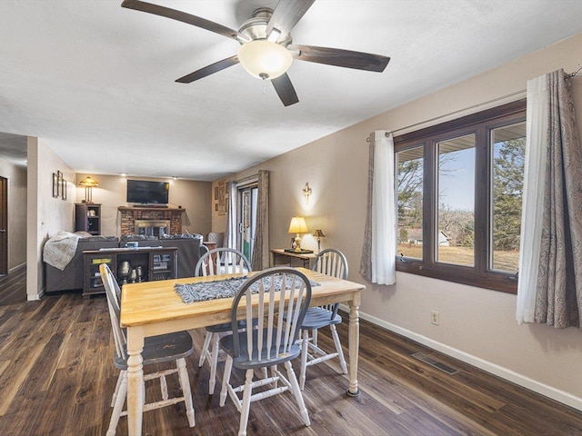 dining area with visible vents, a ceiling fan, dark wood finished floors, baseboards, and a brick fireplace