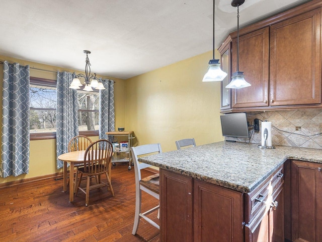 kitchen featuring light stone counters, backsplash, dark wood finished floors, and hanging light fixtures