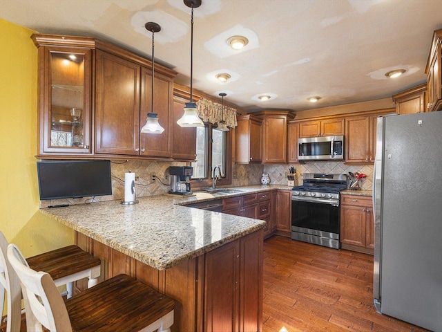 kitchen featuring light stone countertops, a peninsula, a sink, stainless steel appliances, and brown cabinets