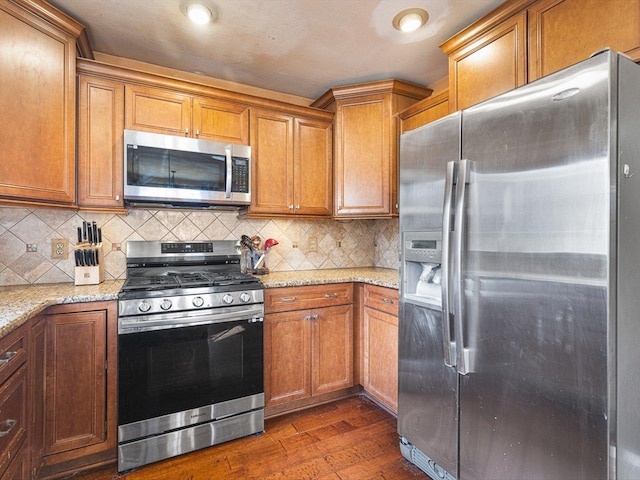 kitchen featuring tasteful backsplash, stainless steel appliances, dark wood-type flooring, and light stone countertops