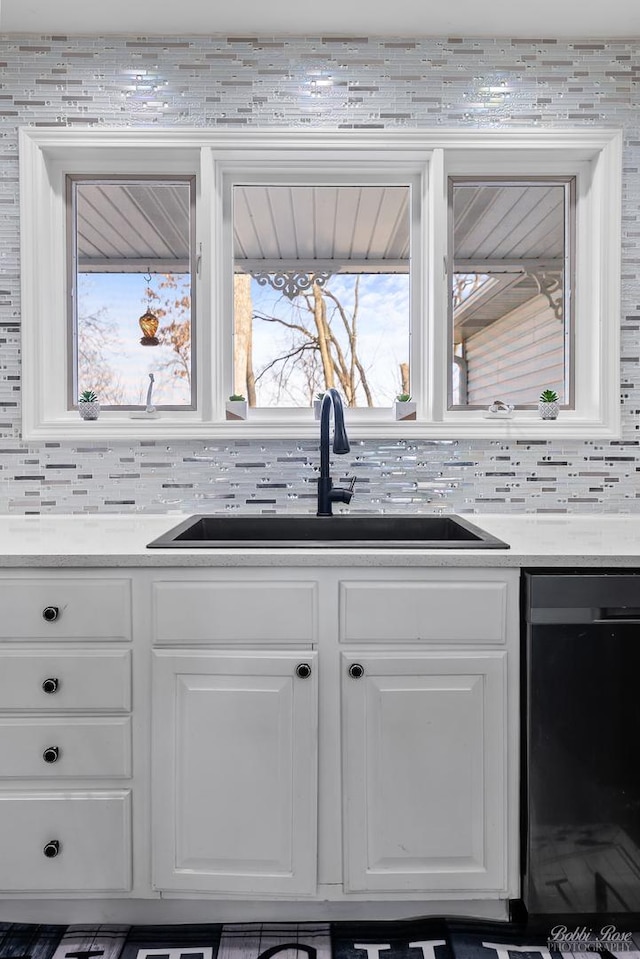 kitchen featuring a sink, white cabinetry, dishwashing machine, light countertops, and decorative backsplash