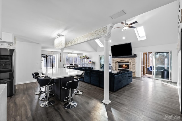 kitchen featuring dark wood finished floors, lofted ceiling, a kitchen breakfast bar, a fireplace, and white cabinetry