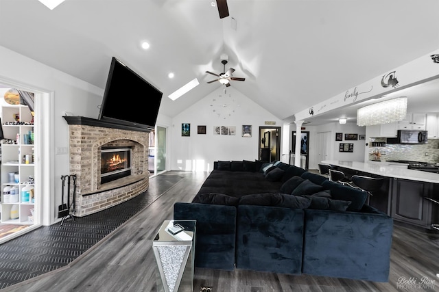 living room with a brick fireplace, ceiling fan, dark wood-style floors, high vaulted ceiling, and ornate columns