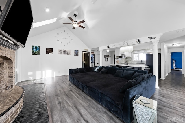 living area featuring high vaulted ceiling, dark wood-type flooring, a ceiling fan, a fireplace, and decorative columns