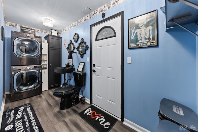 clothes washing area with dark wood-style floors, baseboards, cabinet space, a sink, and stacked washer / drying machine