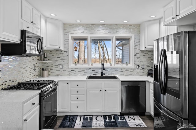 kitchen with black appliances, light countertops, decorative backsplash, white cabinetry, and a sink