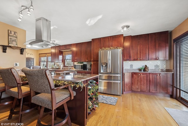 kitchen with island exhaust hood, stainless steel appliances, light wood finished floors, decorative backsplash, and dark brown cabinets