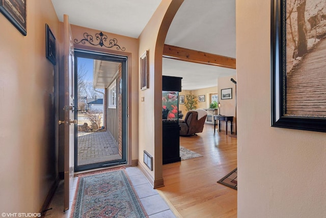 foyer with visible vents, baseboards, beam ceiling, arched walkways, and light wood-style floors