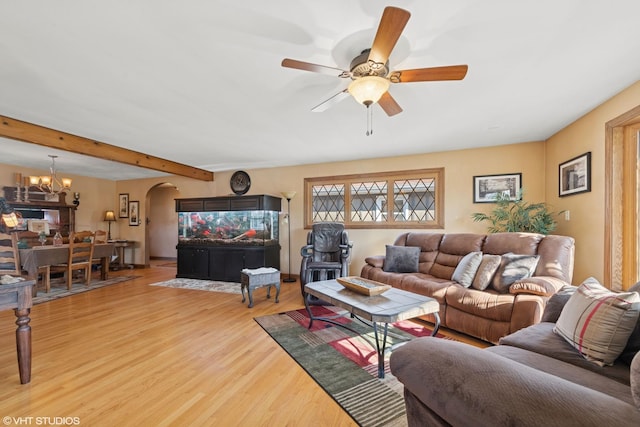 living room featuring arched walkways, beamed ceiling, light wood-style flooring, and ceiling fan with notable chandelier