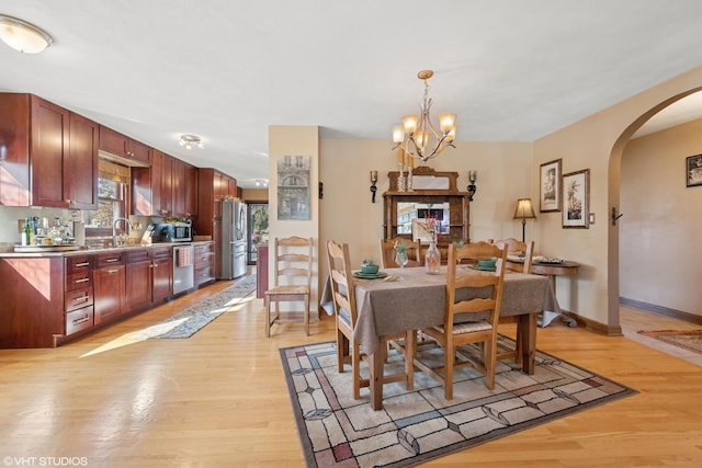 dining area with arched walkways, a chandelier, light wood-type flooring, and baseboards