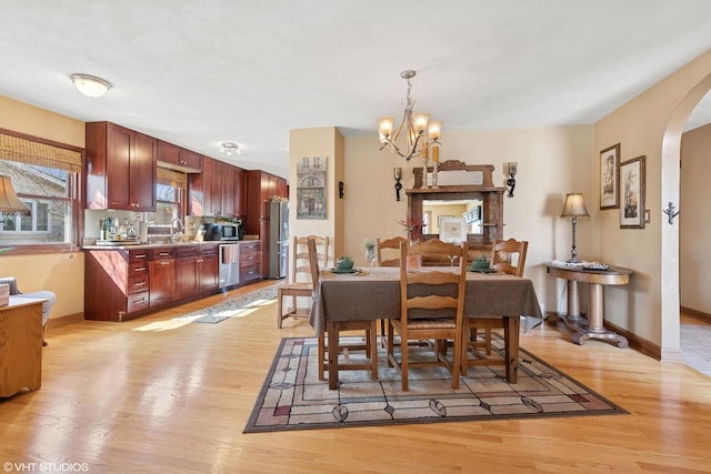 dining area featuring light wood-style flooring, baseboards, arched walkways, and a chandelier