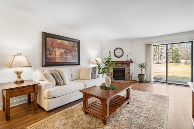 living area with a stone fireplace, wood finished floors, and baseboards