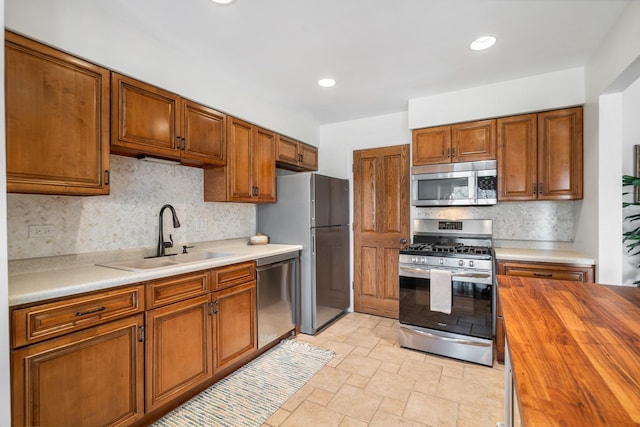 kitchen featuring stainless steel appliances, butcher block counters, backsplash, brown cabinetry, and a sink