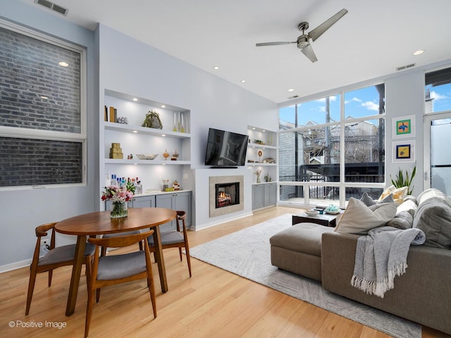 living area featuring light wood-style flooring, visible vents, a wall of windows, and a glass covered fireplace