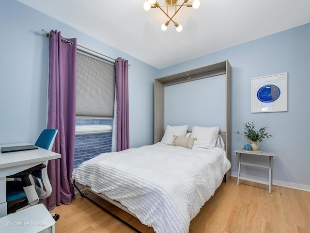 bedroom featuring a chandelier, light wood-type flooring, and baseboards