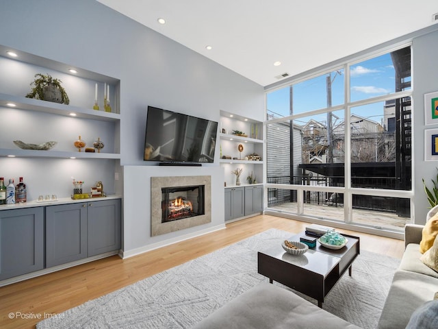 living room featuring built in features, visible vents, a premium fireplace, expansive windows, and light wood-type flooring