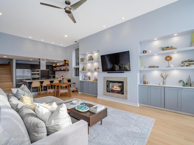 living area featuring built in shelves, light wood-type flooring, a warm lit fireplace, and recessed lighting