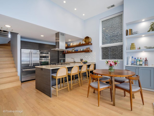 kitchen with a breakfast bar, open shelves, stainless steel appliances, visible vents, and island range hood