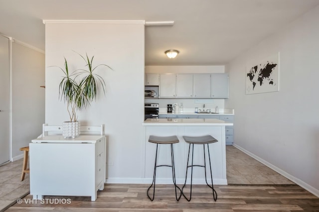 kitchen featuring a breakfast bar, a sink, stainless steel electric stove, a peninsula, and light countertops