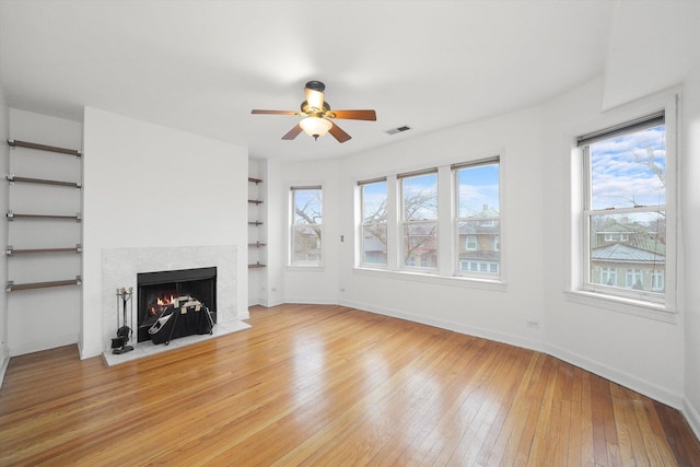 unfurnished living room with light wood finished floors, visible vents, baseboards, and a fireplace with flush hearth