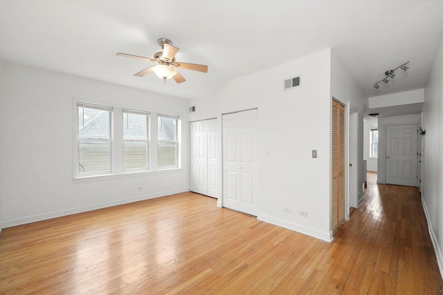 unfurnished bedroom with visible vents, baseboards, multiple closets, light wood-style flooring, and rail lighting