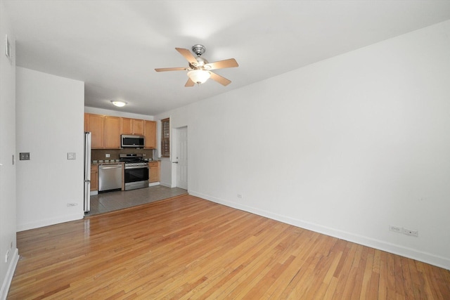 unfurnished living room featuring a ceiling fan, baseboards, and light wood finished floors