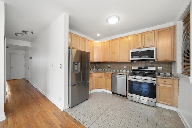 kitchen with light brown cabinets, backsplash, appliances with stainless steel finishes, and baseboards