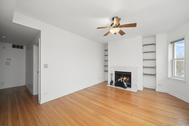 unfurnished living room with light wood-style flooring, a fireplace with flush hearth, visible vents, and ceiling fan