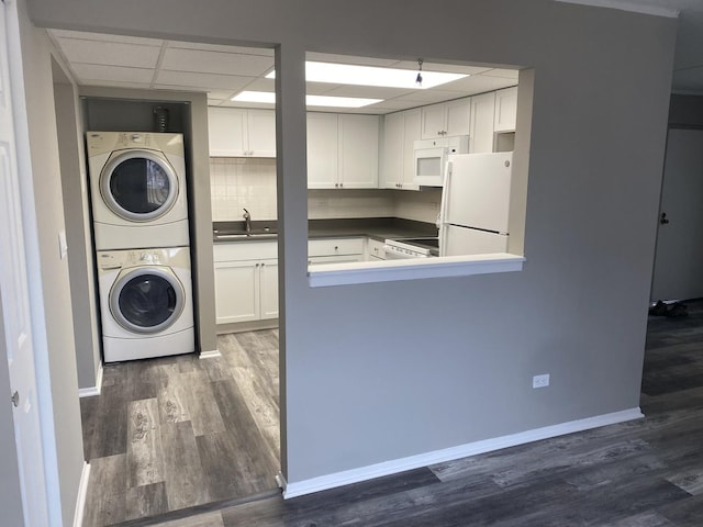 laundry area featuring dark wood-style floors, a sink, stacked washing maching and dryer, laundry area, and baseboards