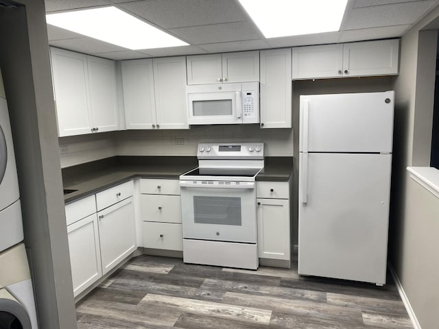 kitchen with dark countertops, white appliances, dark wood-type flooring, and stacked washer / dryer