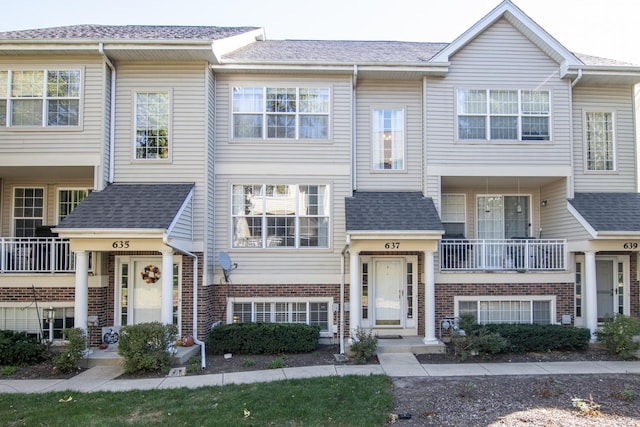 multi unit property featuring roof with shingles and brick siding