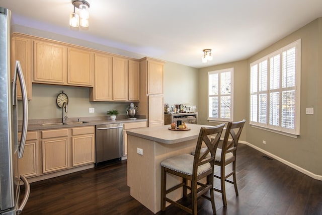 kitchen with a sink, dark wood finished floors, appliances with stainless steel finishes, light brown cabinetry, and a kitchen bar