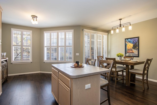 kitchen with dark wood-style floors, a kitchen bar, light countertops, a kitchen island, and baseboards