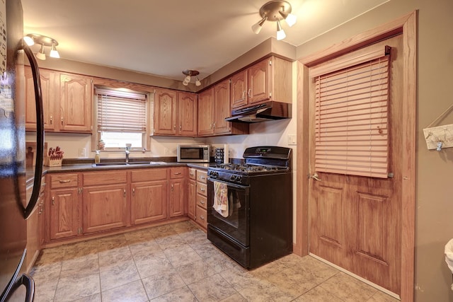 kitchen with brown cabinetry, dark countertops, under cabinet range hood, black appliances, and a sink