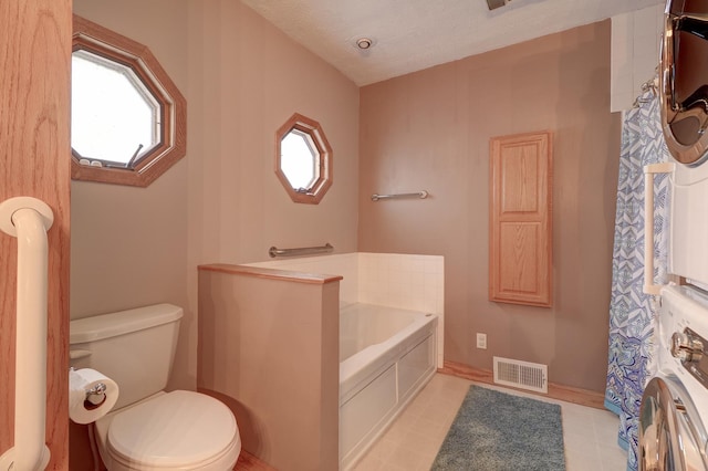 full bath with a garden tub, visible vents, toilet, a textured ceiling, and washer / dryer