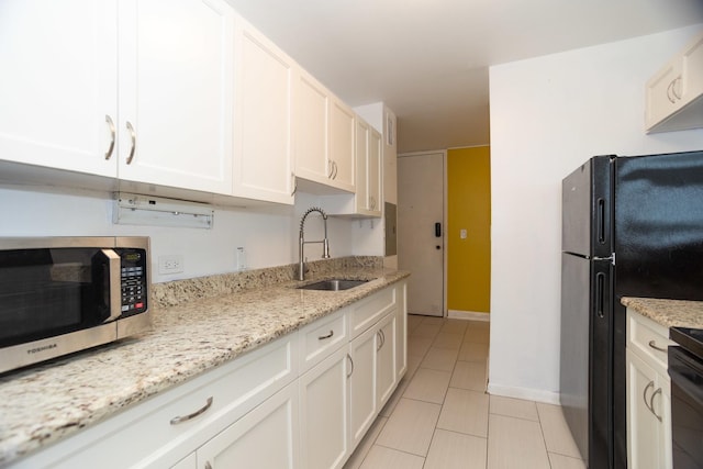 kitchen with stainless steel microwave, a sink, freestanding refrigerator, and white cabinets