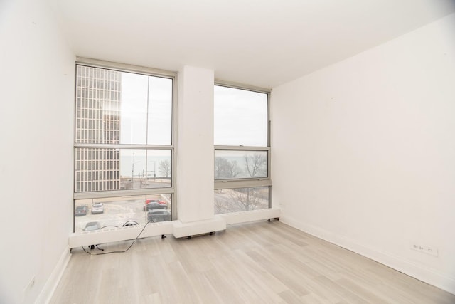 spare room with a wall of windows, baseboards, and wood finished floors