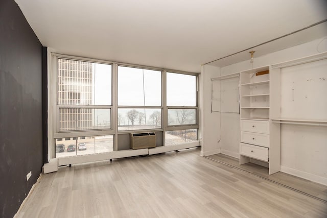 unfurnished bedroom featuring light wood-style floors, a wall mounted air conditioner, floor to ceiling windows, and baseboards