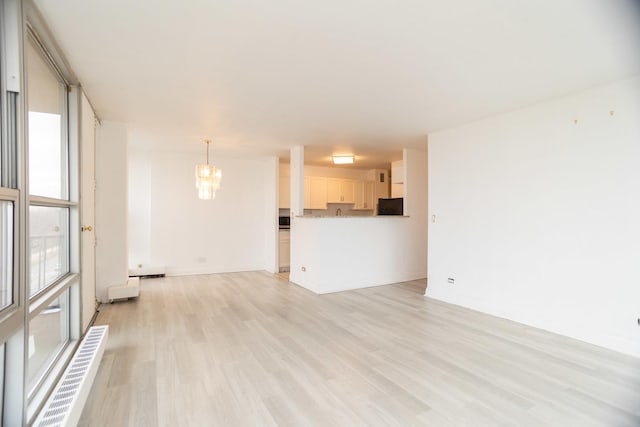 unfurnished living room featuring light wood-style floors, a baseboard heating unit, baseboards, and an inviting chandelier