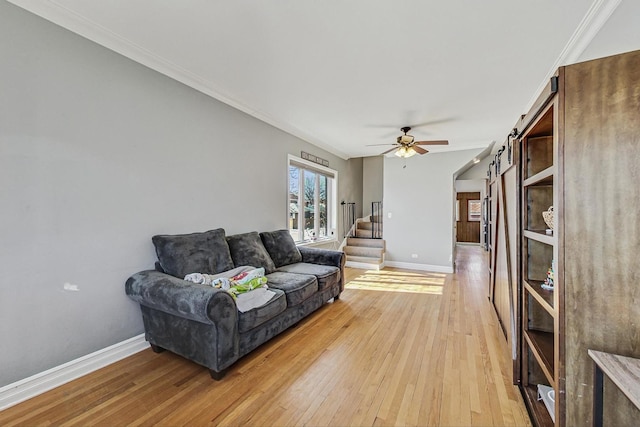 living area featuring ceiling fan, light wood-style flooring, baseboards, and a barn door